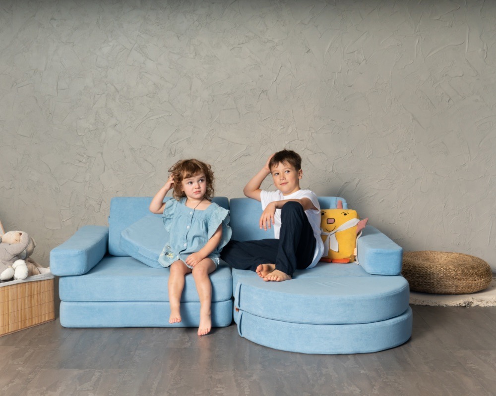 Children are sitting on a blue NUMI hero sofa and thinking about what they are going to build from it